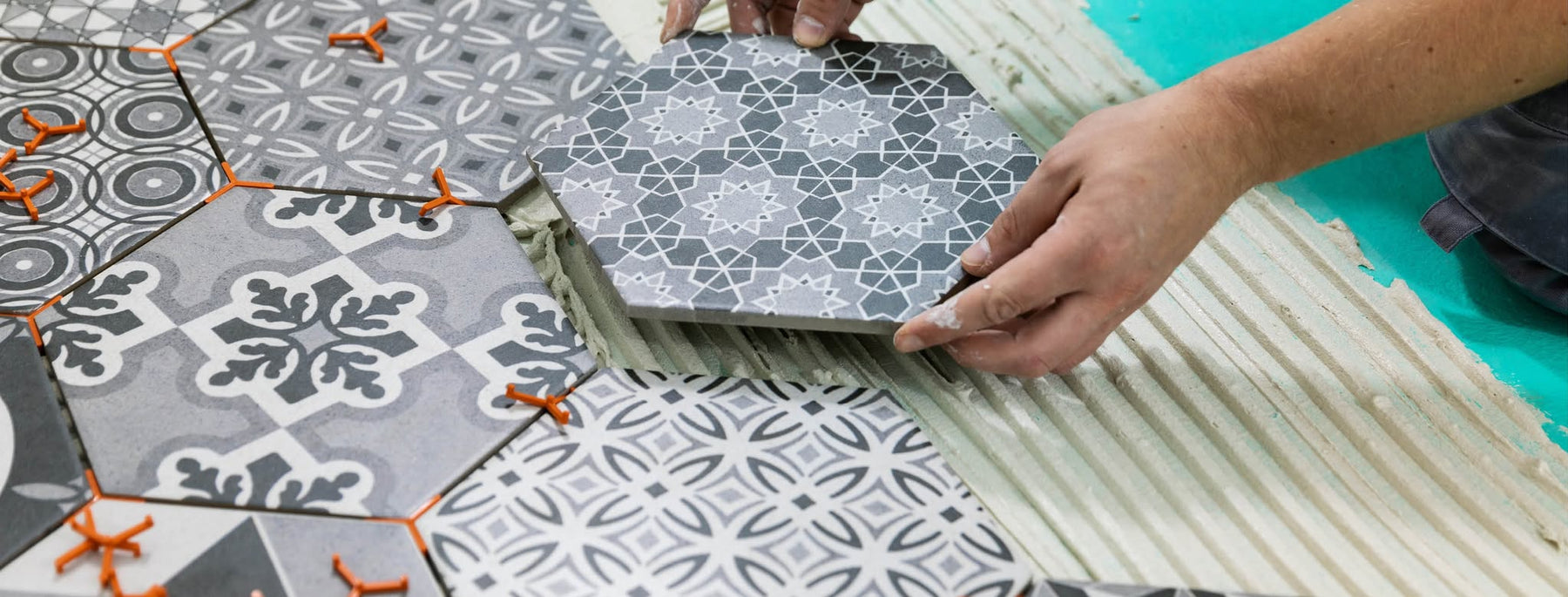 Tiler installing patterned floor tiles using tile adhesive and spacers for precise tile alignment