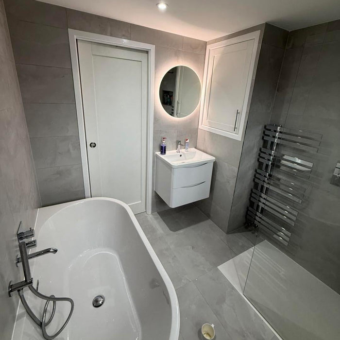 Modern bespoke bathroom designed by Freya featuring a freestanding bath, walk-in glass shower, grey porcelain tiles, wall-hung vanity unit and LED backlit mirror